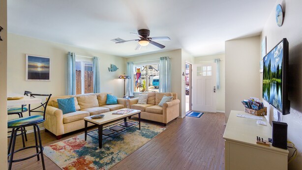 A living room with a beige sofa, a coffee table, a TV, and a ceiling fan. - Bring Your Bag And Get Ready To Relax!! (Oxnard)