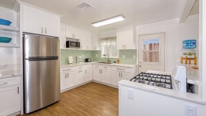 A modern kitchen with white cabinets, a stainless steel refrigerator, a microwave, a gas stove, and a wooden floor. - Bring Your Bag And Get Ready To Relax!! (Oxnard)