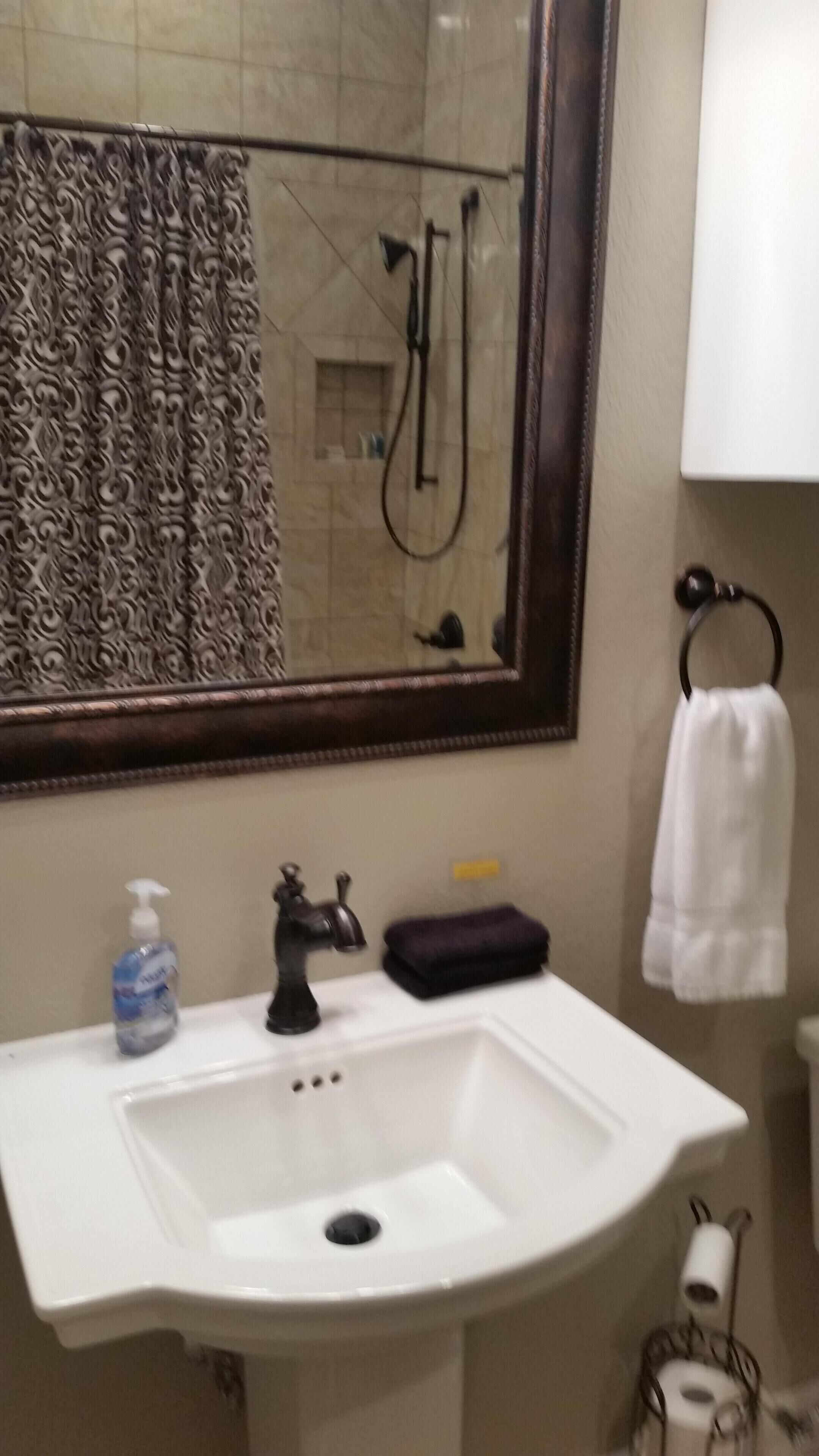 A bathroom with a white sink, a mirror, a shower, and a towel rack.