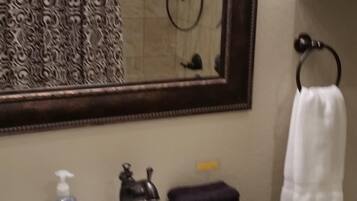 A bathroom with a white sink, a mirror, a shower, and a towel rack.