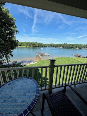 A patio with a mosaic table, a wicker chair, and a view of a lake with boats and a dock.