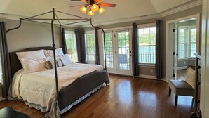 Een ruime slaapkamer met een hemelbed, een plafondventilator en grote ramen.