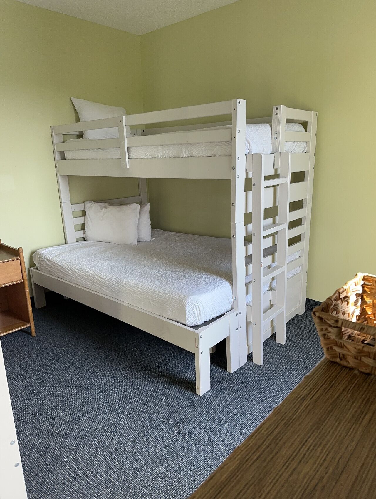 A bunk bed in a room with light green walls, a blue carpet, and a wooden side table.