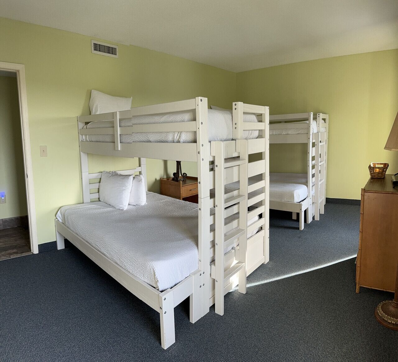 A room with bunk beds, a wooden nightstand, and a lamp.