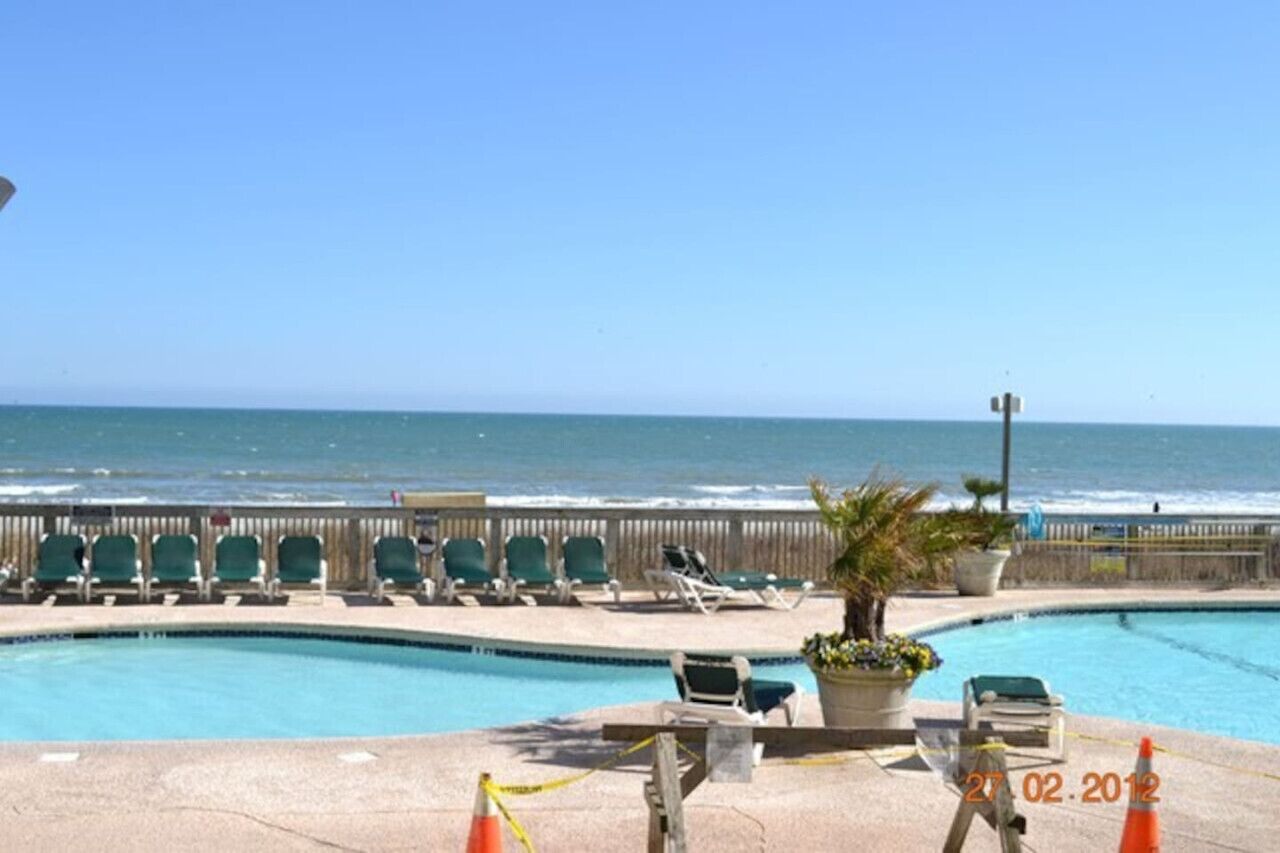 A pool area with lounge chairs and a view of the ocean.