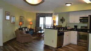 A spacious living room with a sofa, a dining area, and a kitchen with white cabinets and stainless steel appliances.