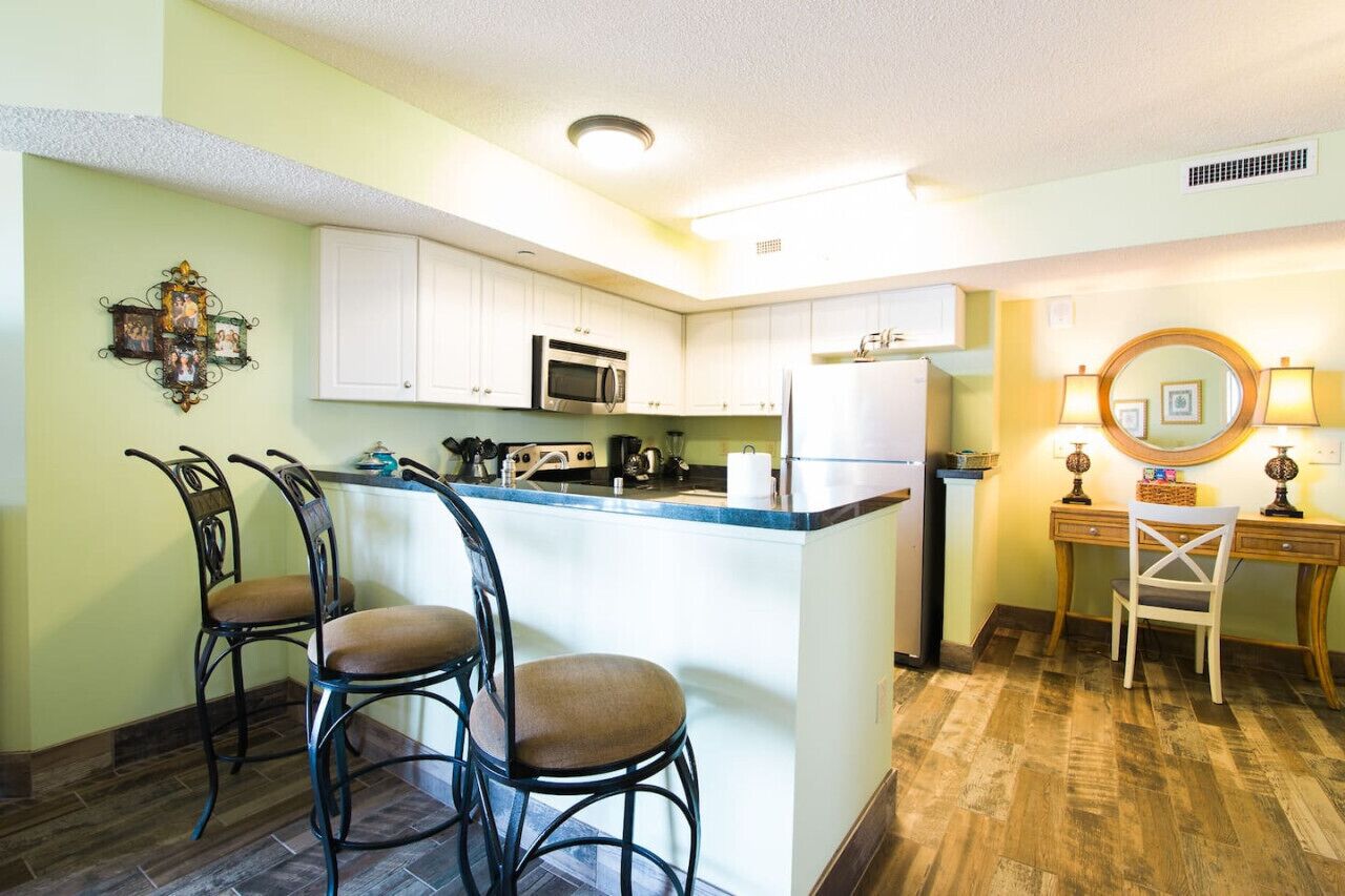 A kitchen with white cabinets, a microwave, a refrigerator, and a bar area with stools.