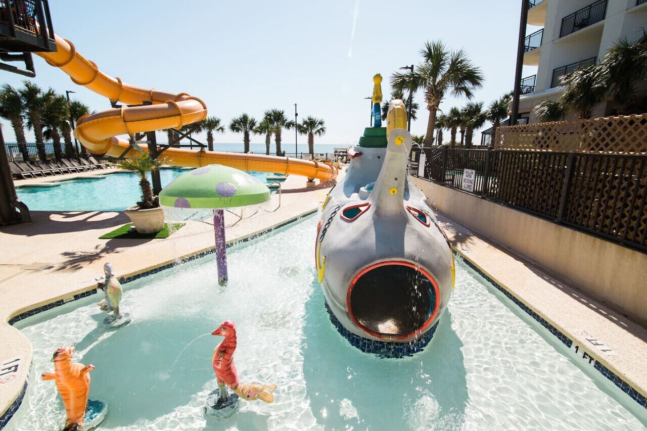 A pool area with a water slide, a large inflatable shark, and palm trees.