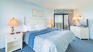 A hotel room with a bed, two bedside lamps, a nightstand, a dresser, a television, and a door with a view.
