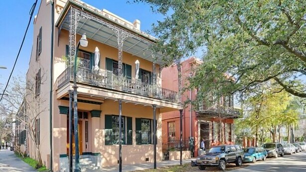 Un immeuble de deux étages doté d’un balcon, d’un porche couvert et donnant sur la rue, où l’on peut voir des voitures garées.