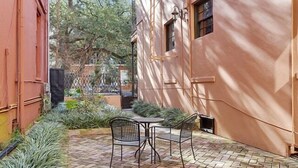 Une cour avec un sol en briques, deux chaises en métal et une petite table.