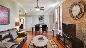 Un salon avec un canapé en cuir, une table basse, un téléviseur et un mur en briques.