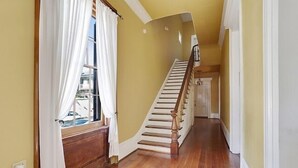 Un escalier avec des marches en bois et une rampe, menant à un palier doté d’une fenêtre et de rideaux.
