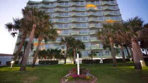 A multi-story hotel with balconies, surrounded by palm trees and a well-maintained lawn.