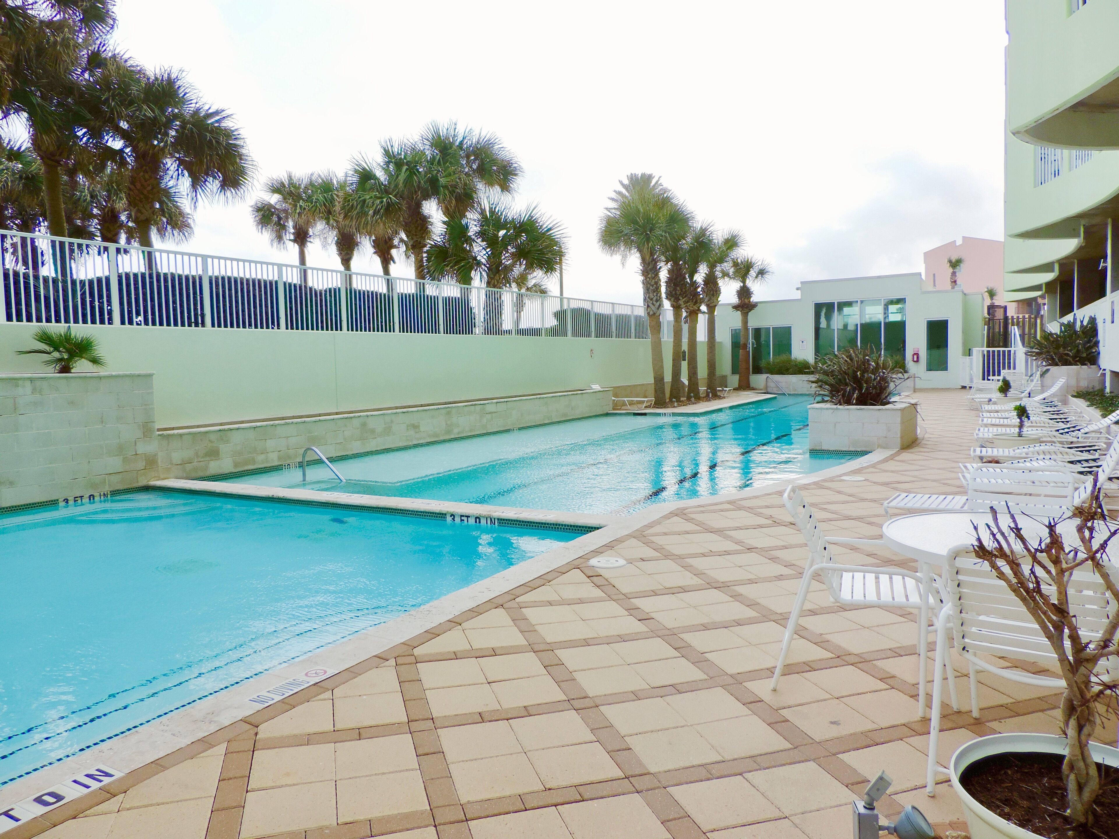 A swimming pool with a tiled deck, lounge chairs, and palm trees.