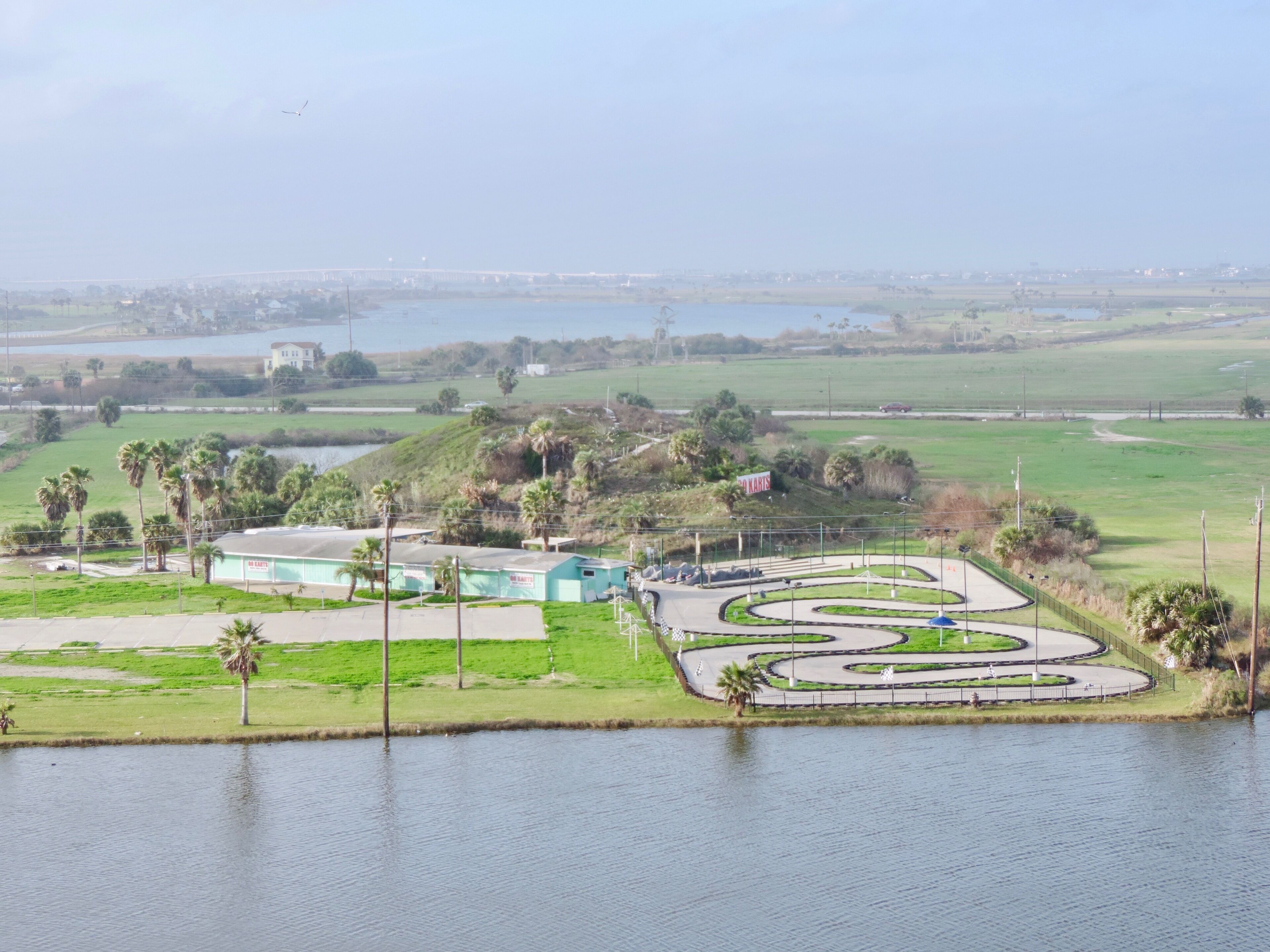 A large, open area with a central landscaped garden, a body of water, and a distant bridge.
