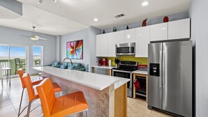 A modern kitchen with white cabinets, stainless steel appliances, and orange bar stools.