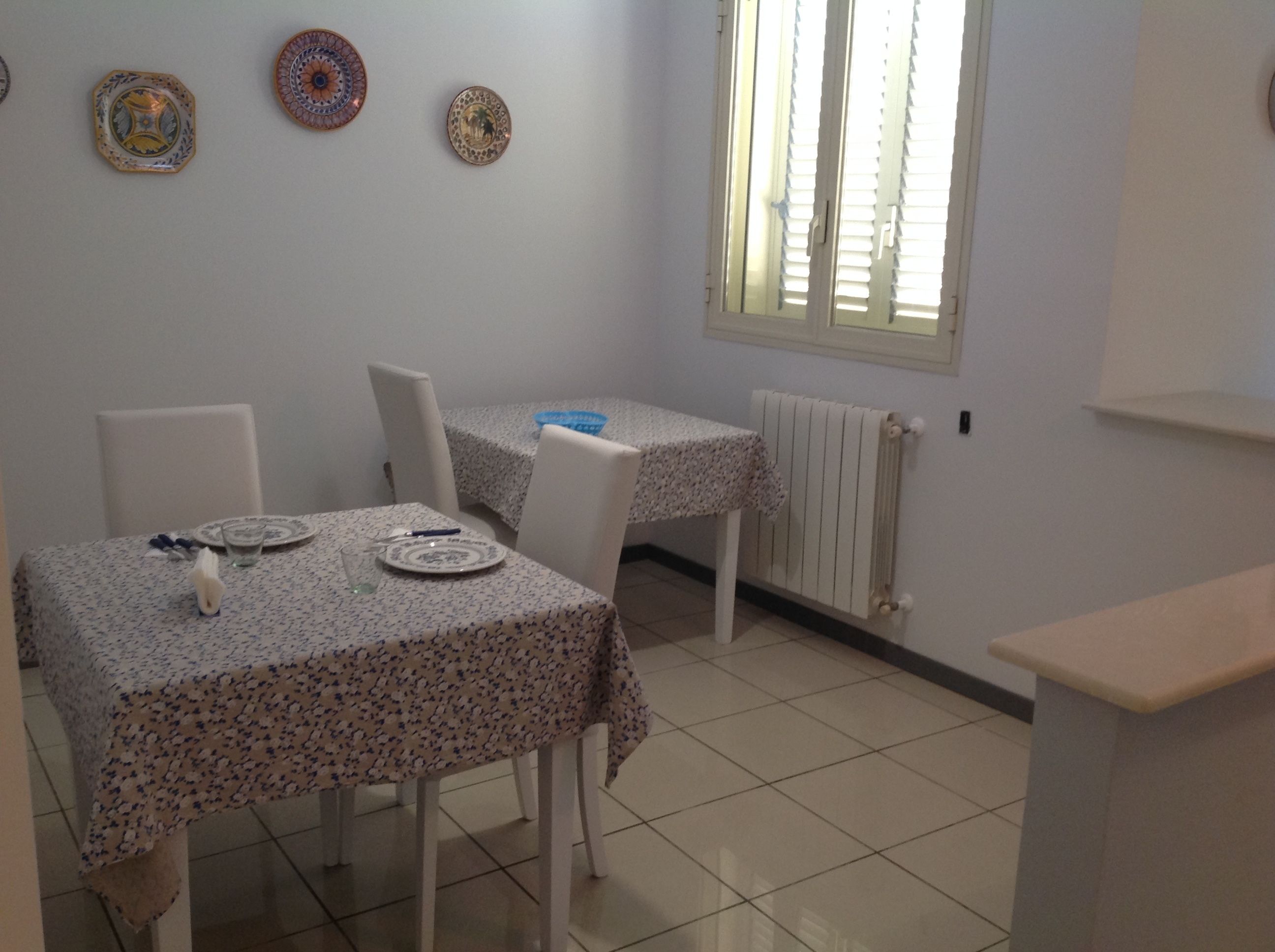 A dining area with a table set for two, a window with blinds, and a radiator.