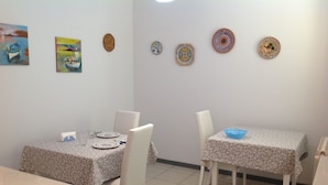 Un comedor con dos mesas, cada una con mantel floral y sillas blancas. Hay platos decorativos en la pared sobre las mesas.