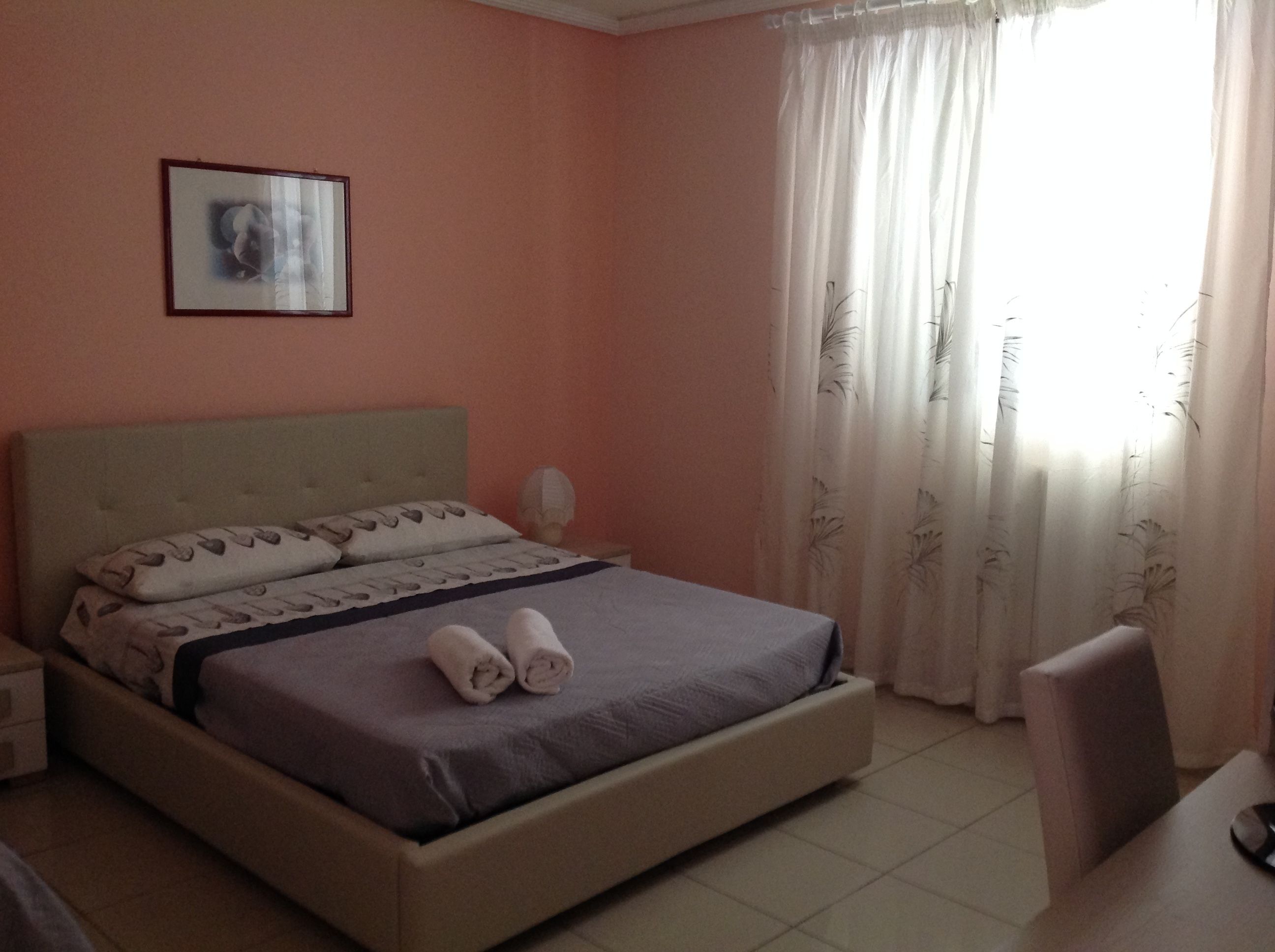 Una cama bien hecha con cabecera, una mesita de noche con lámpara y un cuadro en la pared.