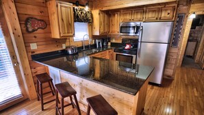 Una cocina de estilo rústico con muebles de madera, una isla central, taburetes de bar, un refrigerador de acero inoxidable y un microondas.