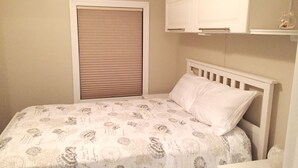 A bedroom with a bed, a window with blinds, a white cabinet, and a small table.