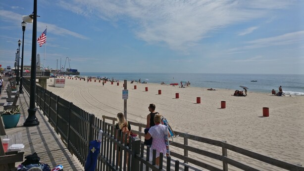A beach with a wooden walkway, red barriers, and a Ferris wheel in the background.