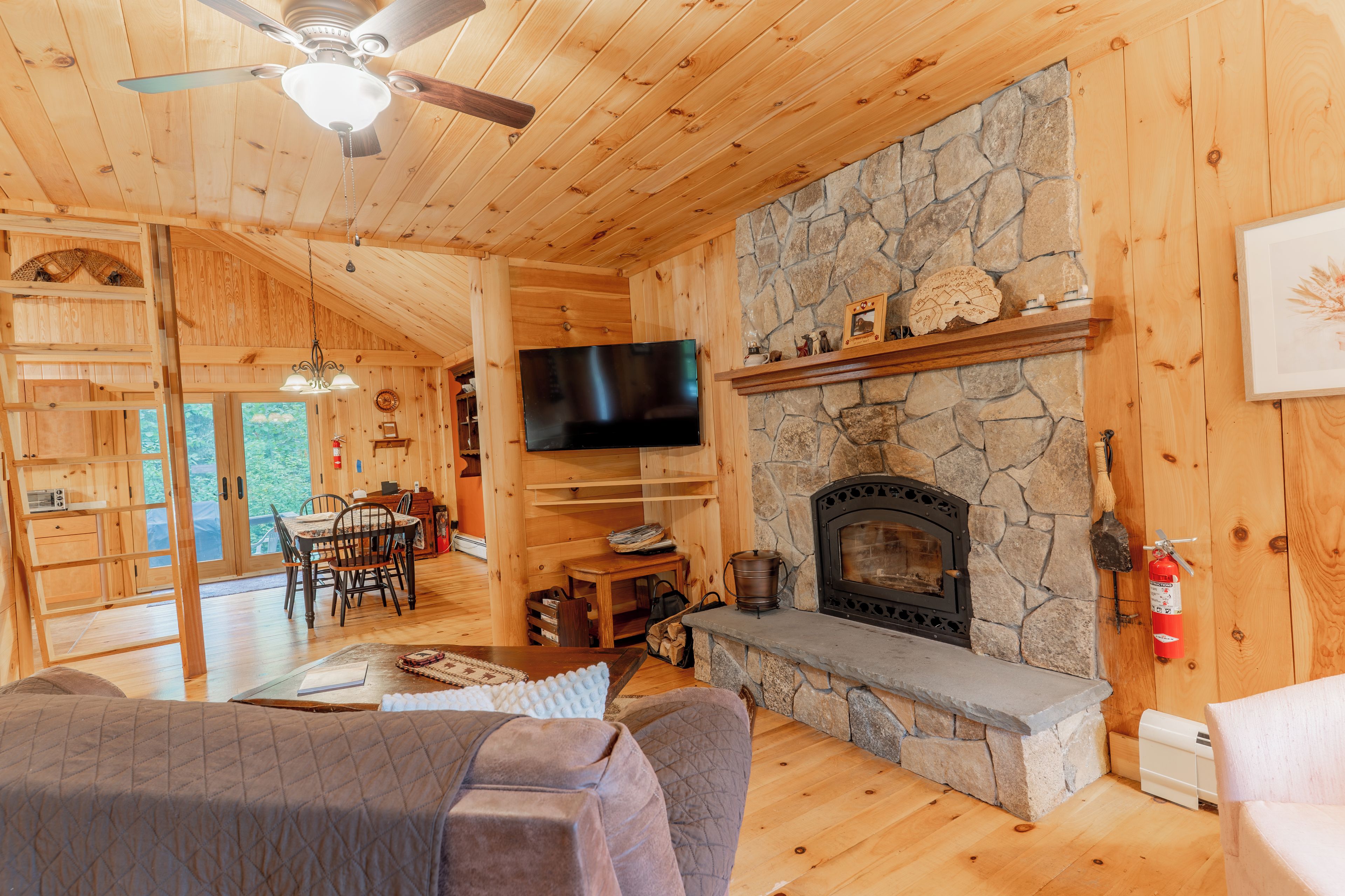 A wooden interior with a stone fireplace, a flat-screen TV, and a dining area with a table and chairs.