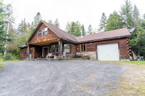A log cabin with a stone foundation, a garage, and a gravel driveway. - Comfy Home in the Adirondacks, close to Gore Mnt, hiking & snowmoble trails (Indian Lake)
