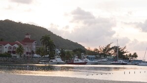 Un port de plaisance avec des bateaux amarrés, une plage au premier plan et des bâtiments aux toits rouges en arrière-plan.