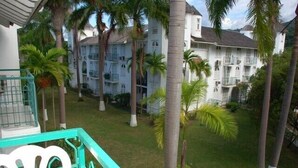 Une cour d’hôtel à plusieurs étages, agrémentée de palmiers et d’une pelouse verdoyante.