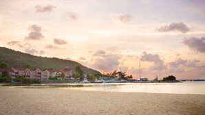 Une plage bordée d’une rangée d’immeubles d’hôtel, une mer calme et un pont visible au loin.