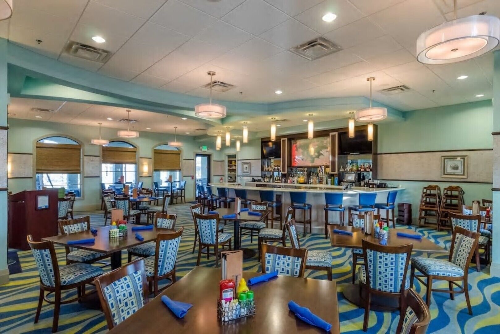 Een hotel lobby met verschillende eettafels, stoelen, een bar en een groot scherm waarop een kaart wordt weergegeven.