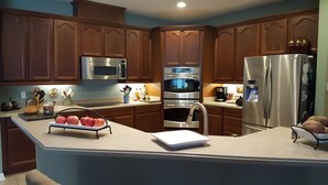 A modern kitchen with wooden cabinets, stainless steel appliances, and a central island with apples and a notebook.