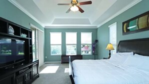 A bedroom with a bed, a TV, a ceiling fan, and a window with blinds.