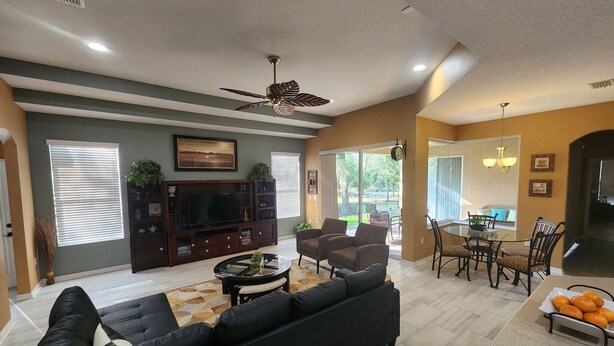 A spacious living room with a large black sofa, a flat-screen TV, and a ceiling fan.