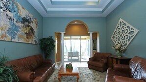 A living room with a brown leather sofa set, a wooden coffee table, and a patterned rug. There is a large painting on the wall and a decorative wall piece.