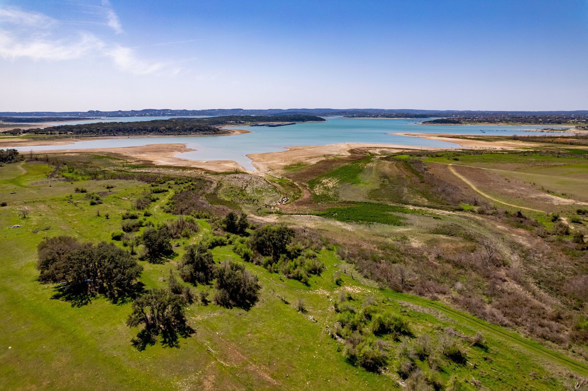 Vista aérea de un paisaje costero con una extensa masa de agua, campos verdes y árboles dispersos.