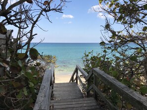 A wooden staircase leading to a beach with clear blue water and a wooden railing. - Seashell 1- Luxury Studio close to the beach (Boynton Beach)