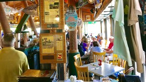 Interno di un ristorante con travi in legno, una lavagna con il menù e vista sulla spiaggia.