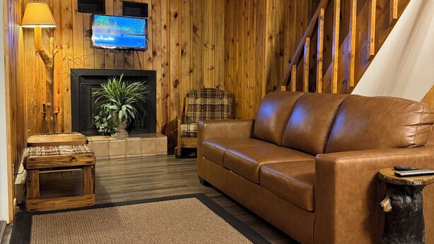 A cozy living room with a wooden wall, a leather sofa, a fireplace, a television, and a staircase. - Double Diamond Lodge on Terry Peak--Your outdoor adventures await!! (Lead)