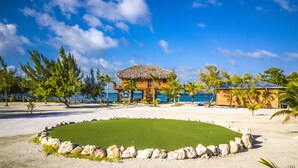 A beachside resort with a thatched-roof building, a pool, and a view of the ocean. - All INCLUSIVE BELIZE PRIVATE ISLAND RENTAL WITH OVER WATER BUNGALOW AND CHEF (Belize City)