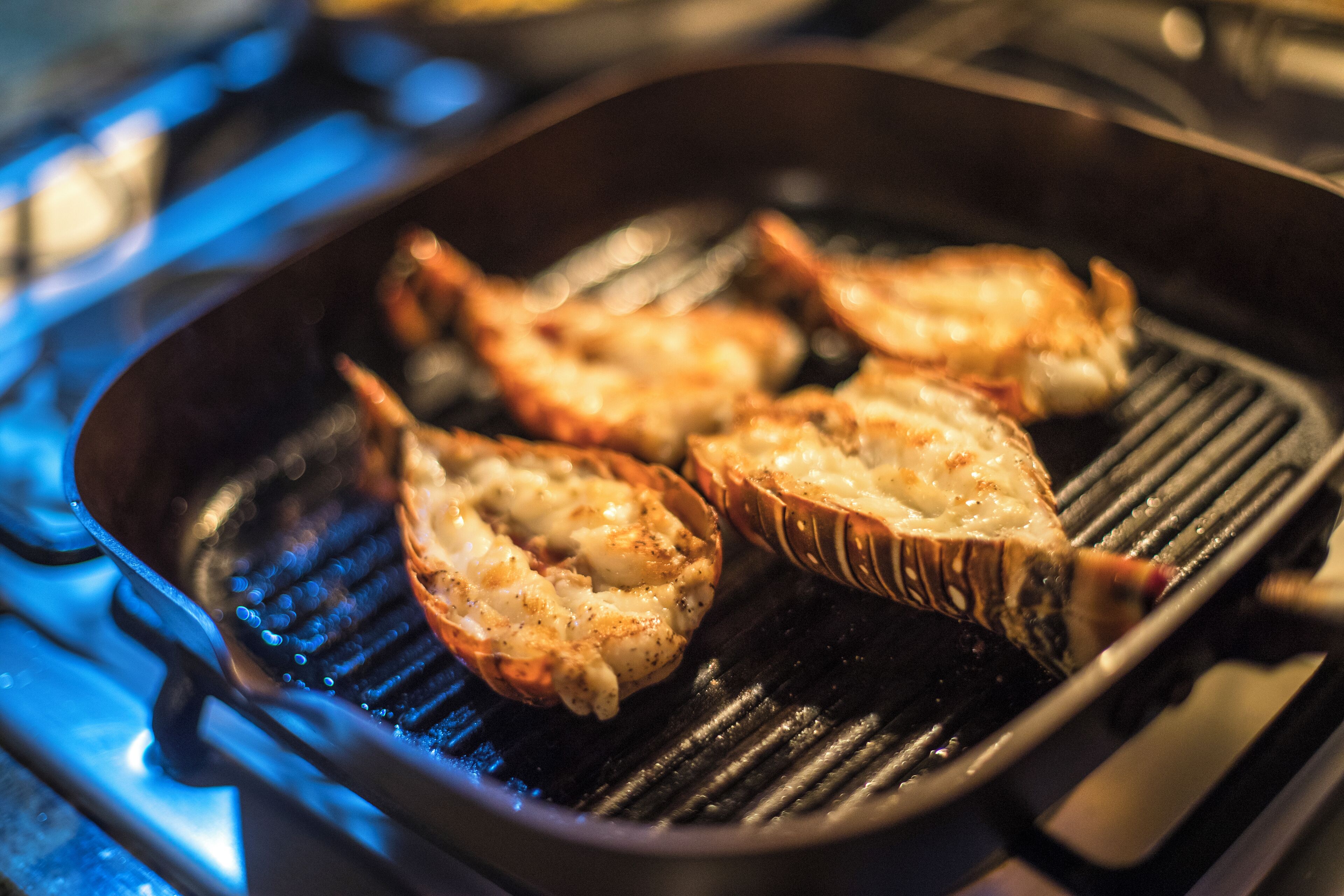 Gros plan sur des queues de homard grillées sur une plaque de cuisson.