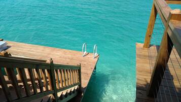 A wooden deck with metal pool ladders leading into clear turquoise water.