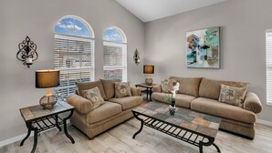 A living room with a beige sofa set, two side tables, a coffee table, and a painting on the wall. - Ashland Palms: Modern pool home, close to Disney on Glenbrook Resort  (Clermont)