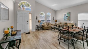 A spacious living room with a dining area, a sofa set, and a large window with a view. - Ashland Palms: Modern pool home, close to Disney on Glenbrook Resort  (Clermont)