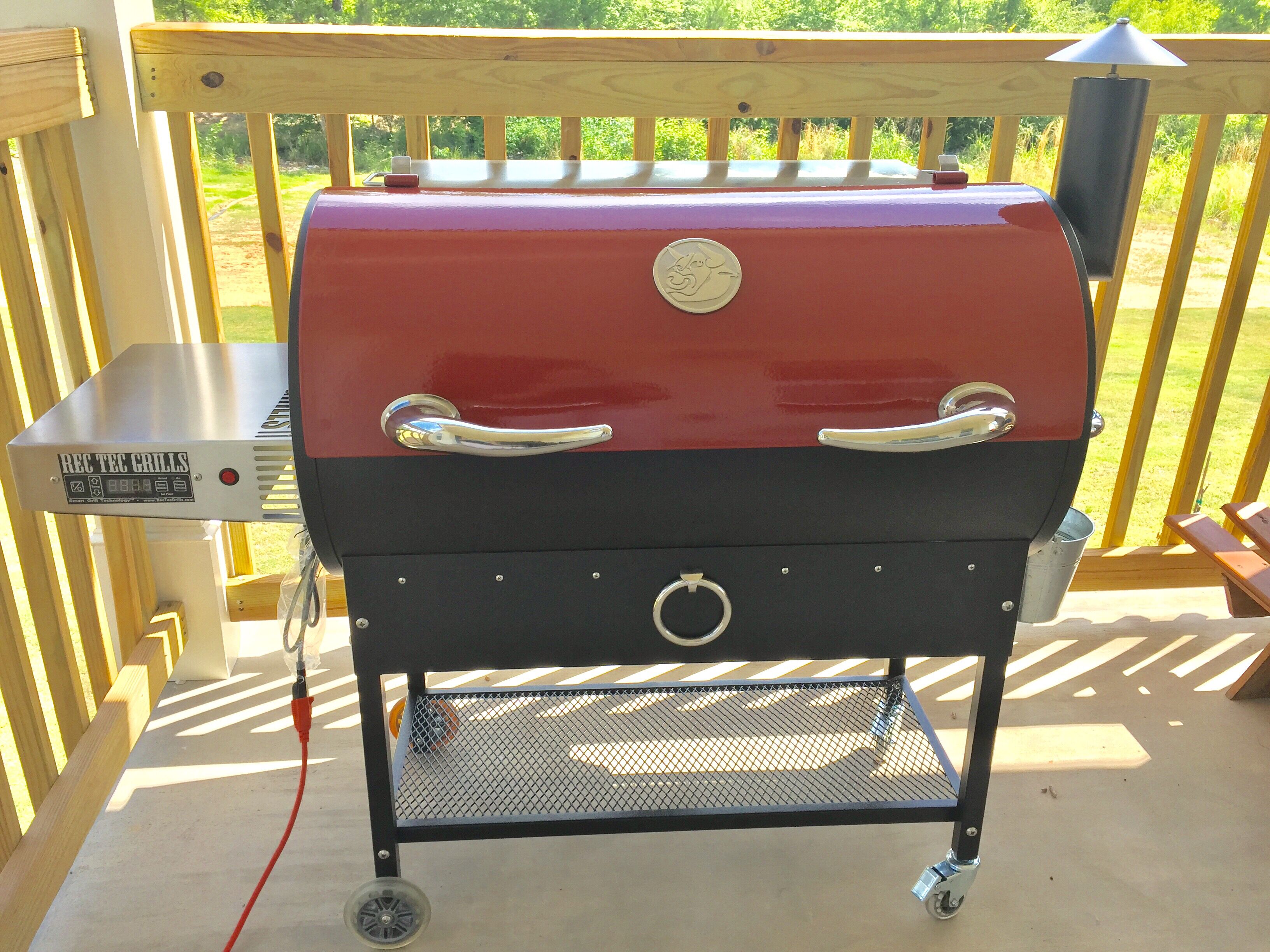 Ein Grill mit Holzkohle auf einer Holzterrasse, dazu ein Grillwagen aus Metall.