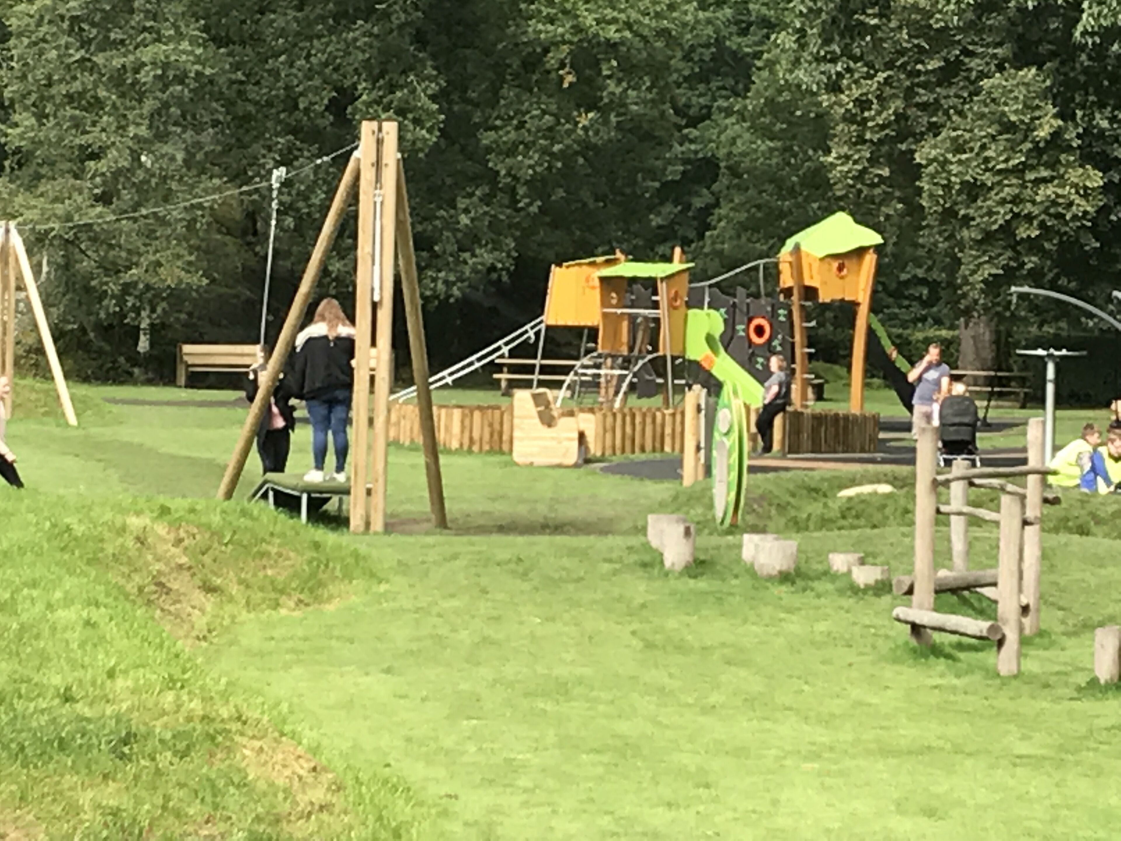 En legeplads med forskellige legevenlige konstruktioner, herunder gyngestativ, klatrestige og rutchebane.