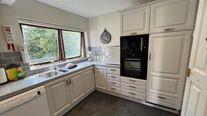 Una cocina moderna con armarios blancos, un lavavajillas Bosch, un horno empotrado y una ventana con cortinas.