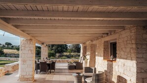 Une terrasse extérieure avec des piliers en pierre, des meubles en osier et un mur en pierre.